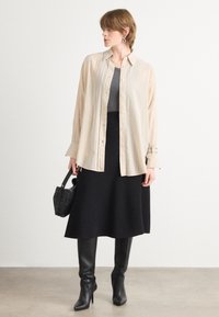 Beige button-up shirt with vertical stripes, gray fitted top, black skirt, knee-high boots, and a textured black handbag.