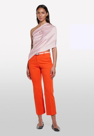 Helles rosa drapiertes Oberteil, orangefarbene enganliegende Hose mit einem weißen Gürtel und schwarze Ballerinas. Das Outfit zeichnet sich durch eine glatte Textur und eine moderne Silhouette aus.