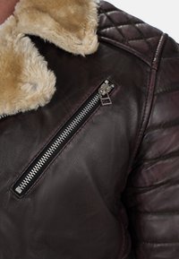 Giacca in pelle marrone con motivo trapuntato sulle spalle, colletto in shearling e tasca con zip dettagliata in metallo argento.