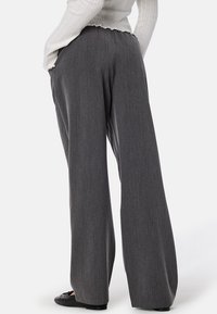 Grijze, wijde broek met een gladde, gestructureerde stof en elastische tailleband, met een subtiel patroon. Zwarte schoenen maken de look af.