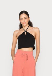 Top cropped preto com alças e um detalhe em forma de buraco na frente, combinado com calças rosa claro com cordão, feitas de um tecido macio.