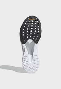 Suela de zapato de goma negra con un patrón texturizado y entresuela blanca. Presenta un marcado branding y un diseño ligero.