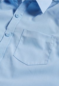 Chemise bleu clair à boutons, en tissu lisse avec un col pointu, dotée d'une petite poche sur la poitrine à gauche.