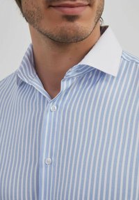 Chemise à rayures bleu clair et blanche avec un col blanc, comportant deux boutons et une texture de tissu lisse.