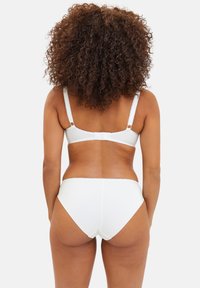 Ensemble de lingerie blanche comprenant un soutien-gorge avec des bretelles réglables et des bords festonnés, associé à des culottes taille haute, texture lisse, coupe ajustée.