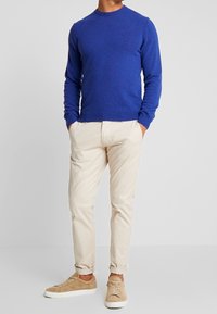 Blå crewnecktröja, beige chinos och ljusbruna sneakers. Tröjan har ett strukturerat tyg med ribbade muddar och nederkant.