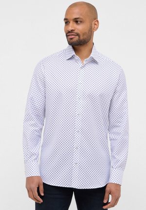 Witte button-up blouse met een geometrisch marineblauw patroon, lange mouwen, puntige kraag en een zachte textuur, gecombineerd met donkerdenim jeans.