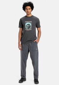 Gray cotton T-shirt with mountain graphic and text, paired with dark gray cargo pants featuring side pockets and a logo. Black sneakers.