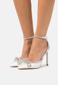 White satin high-heeled shoes with pointed toes, embellished with a rhinestone-accented bow and ankle straps featuring crystal detailing.