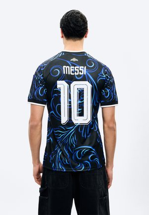 Νεαρός άνδρας που φαίνεται από πίσω, φοράει μια μαύρη και μπλε ποδοσφαιρική φανέλα με σχέδια, με την επιγραφή «Messi» και τον αριθμό 10 σε λευκό στο πίσω μέρος.