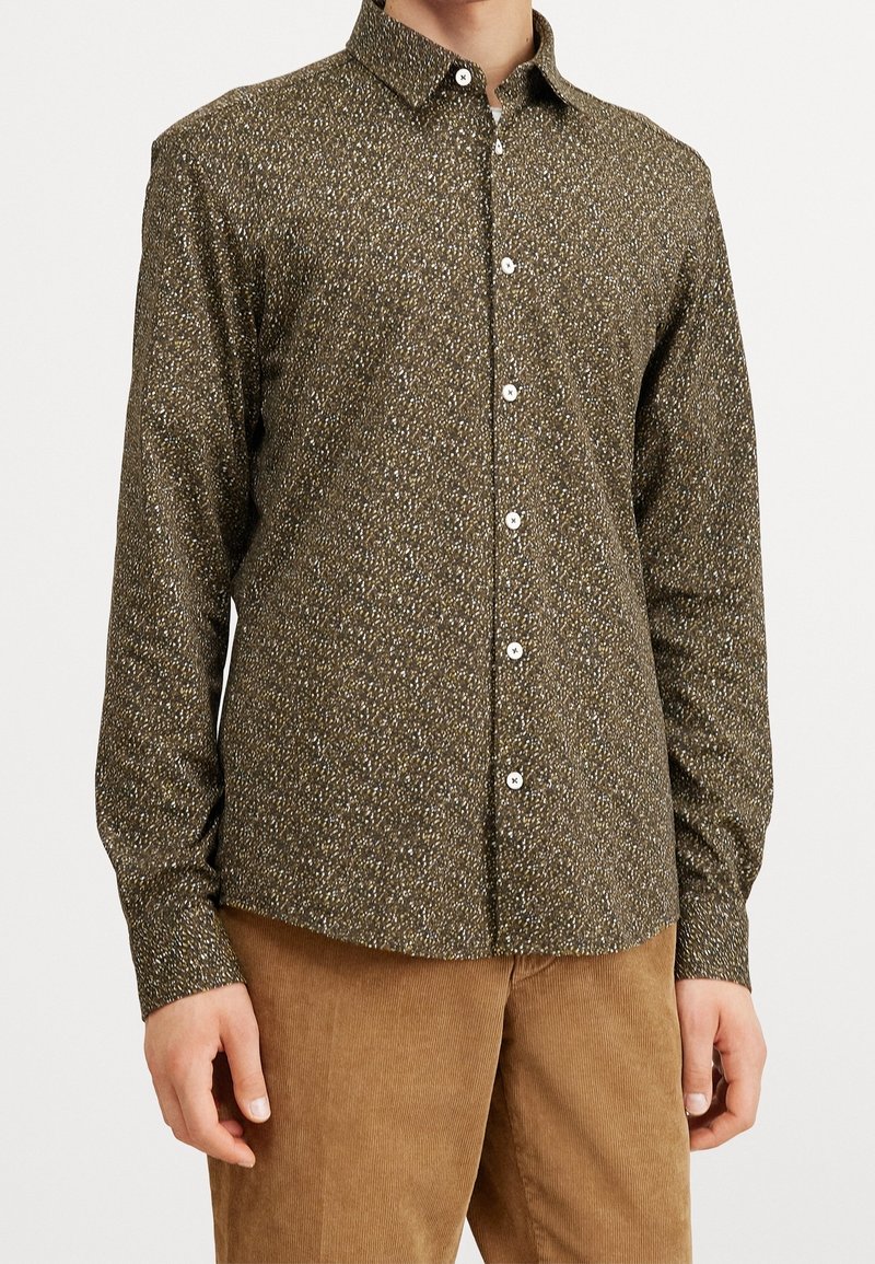 Camicia a maniche lunghe marrone con motivo, arricchita da piccole macchie bianche e verdi, colletto button-down e bottoni bianchi, abbinata a pantaloni in corduroy beige.