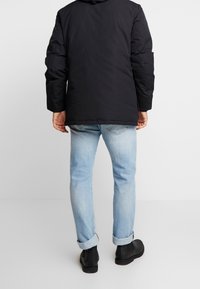 Sort polstret jakke med hætte, kombineret med lyseblå opkrebede jeans og sorte ankelstøvler. Simpelt design, uden synlige mønstre.