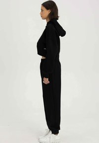 Zwart cropped hoodie met een capuchon en elastische onderrand, gecombineerd met bijpassende zwarte joggingsbroek. Witte sneakers met textuurdetails.