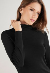 Schwarzes langärmliges Top mit Rollkragen aus einem glatten, dehnbaren Stoff. Verfügt über ein enganliegendes Design mit hohem Kragen und dezenten Nähdetails.