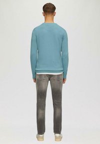 Helles blaues Langarmshirt mit Rundhalsausschnitt, kombiniert mit ausgewaschenen grauen Jeans und beigen Sneakers. Glatte Textur, lässige Passform, schlichtes Design.