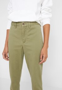 Olive green trousers with a straight cut, made of a cotton blend fabric. Features a front button closure and side pockets.