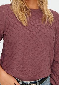 Strickpullover in Mauve mit einer strukturierten Oberfläche, die ein Schuppenmuster aufweist. Rundhalsausschnitt und gerippter Saum, kombiniert mit einem hellblauen Denim-Bund.
