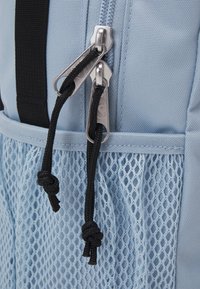 Light blue backpack featuring a mesh pocket, dual silver zippers with black cord pulls, and a textured fabric mesh detail at the bottom.