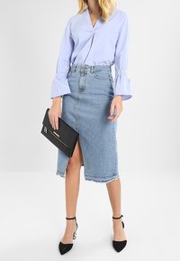 Blusa azzurro chiaro con maniche a campana arricciate, abbinata a una gonna a matita in denim a vita alta con spacco frontale e orlo sfilacciato. Clutch nera e tacchi.