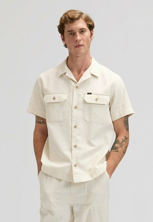 Camicia avorio a maniche corte in tessuto leggero con due tasche sul petto, bottoni in legno e collo dal design rilassato.
