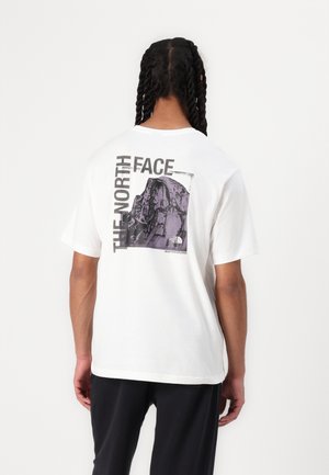Camiseta blanca de manga corta con un gran gráfico morado de una montaña en la parte posterior y el texto "THE NORTH FACE". Material de algodón, corte relajado.
