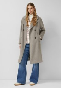 Grijze wollen dubbelgeknoopte jas met grote zwarte knopen, een kraag met inkepingen, oversized pasvorm, gecombineerd met een geruit overhemd en wijde jeans.