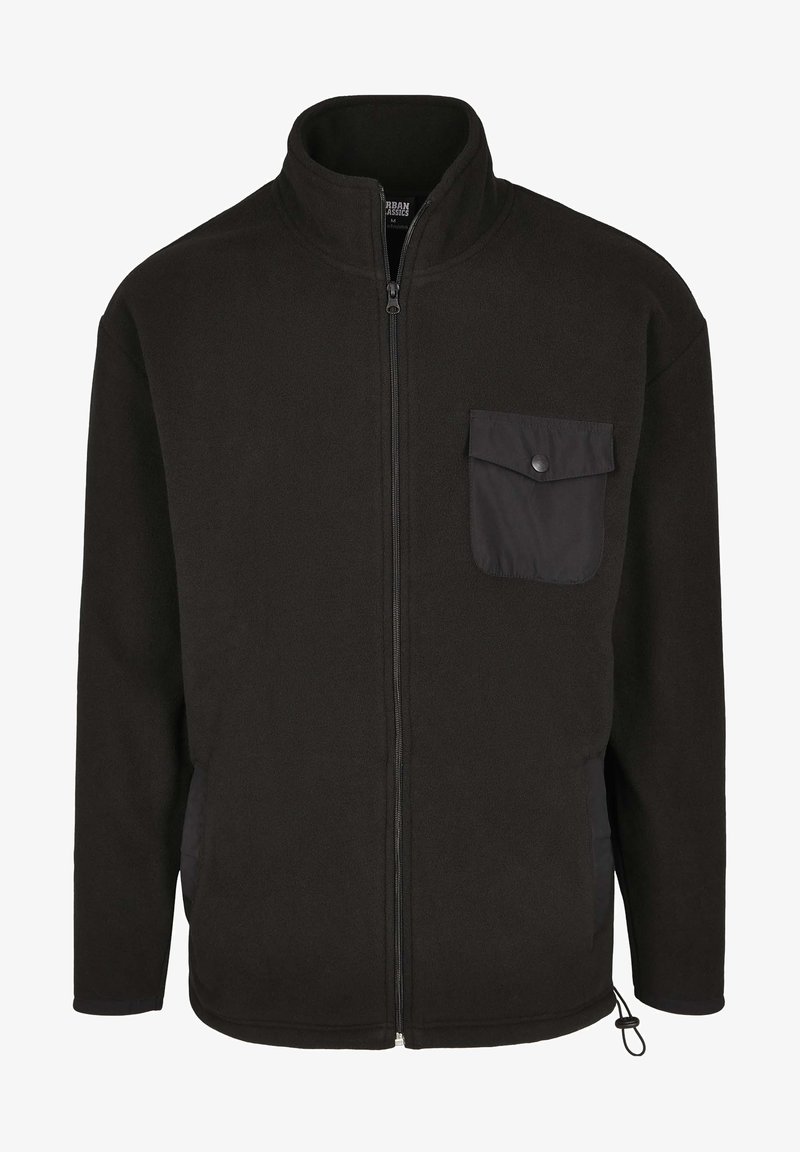 Mustra musta bleiser, millel on kõrge krae, ees lukuga ja nööbiga tasku. Omab küljetaskuid ja kohal on kinnitusnöör.