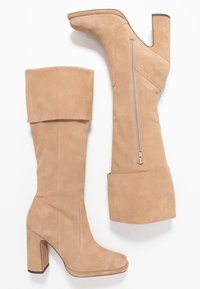 Bottes beige en daim au-dessus du genou avec un revers plié, un talon bloc épais et un détail de fermeture éclair sur le côté. Texture lisse et design élégant.
