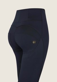 Tummat korkeavyötäröiset leggingsit, joissa on sileä rakenne, kaarevat saumat ja pieni kultainen logoyksityiskohta takana. Varustettu viilto-taskuilla.