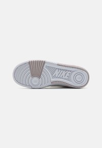 Nike tenisica s potplatom u svijetlosivoj i bež boji, koja sadrži okrugle i utore, teksturirana guma i istaknuti logo.