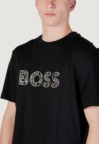 Zwarte katoenen t-shirt met een grote, gestructureerde witte "BOSS" grafiek op de voorkant. Ronde halslijn en korte mouwen.