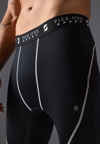 Black athletic leggings with a fitted design, featuring white stitching accents, a branded black waistband, and a smooth texture.