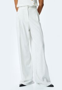 Pantalones de pierna ancha de tela ligera, con rayas verticales en blanco y negro, cintura alta y pliegues frontales para mayor textura.