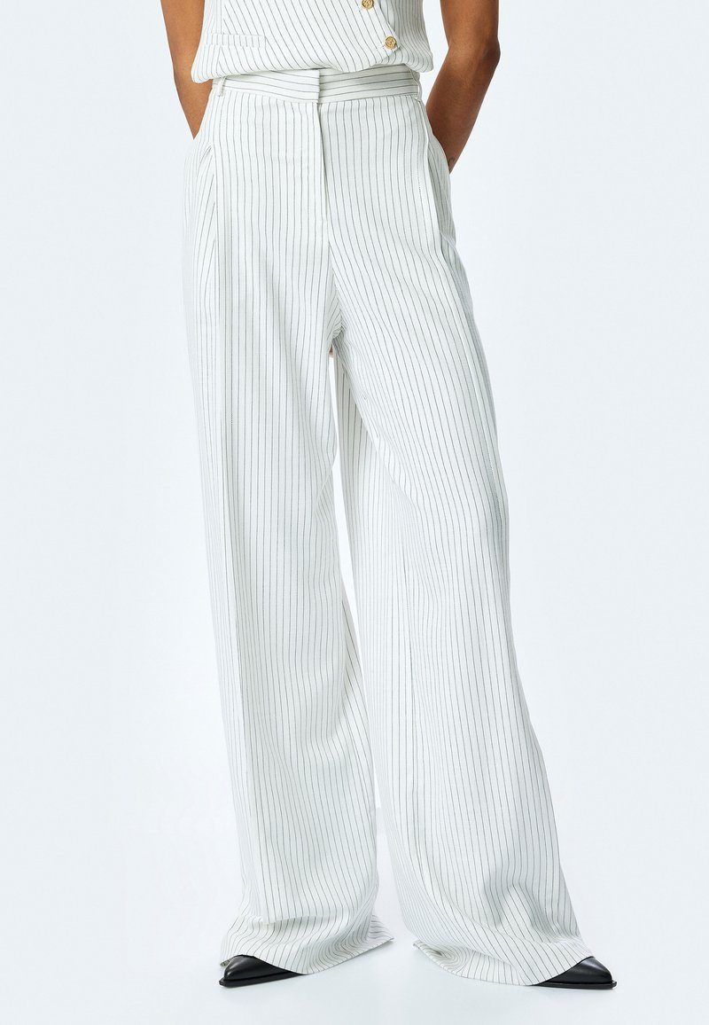 Pantalones de pierna ancha de tela ligera, con rayas verticales en blanco y negro, cintura alta y pliegues frontales para mayor textura.