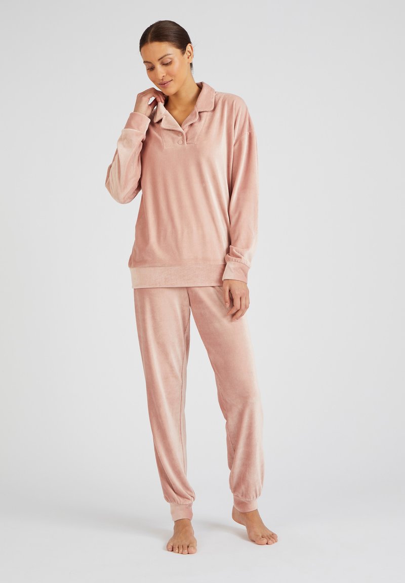 Conjunto de loungewear de terciopelo en rosa suave. Presenta una camiseta de manga larga con cuello y pantalones ajustados en los tobillos, mostrando una textura suave y un corte relajado.