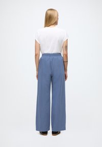 Ljusblå vida byxor med resår i midjan, matchade med en enkel vit kortärmad topp, sedd bakifrån.