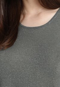 Grå, kortärmad, glittrande stickad topp med rundad halsringning. Tyget har en metallisk lyster med en slät textur.