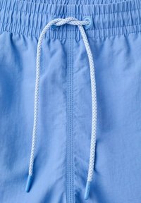 Shorts en tissu bleu clair avec ceinture élastique et cordon blanc tressé noué en un simple nœud au centre avant.