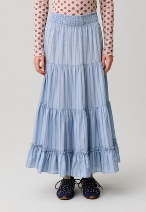 Gonna lunga azzurra chiaro a balze con righe verticali indossata con top floreale e sneakers blu scuro, mostrata dalla vita ai piedi.