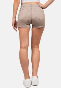 Beige denim shorts met achterzakken, rafelige zoom en riemlussen, gecombineerd met witte sneakers. Zichtbare huidtinten reflecteren natuurlijk licht.