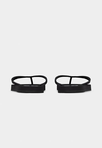 Paire de sandales plates noires avec des lanières fines, design minimaliste et orteils ouverts, posées côte à côte sur un fond blanc.