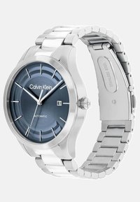 Calvin Klein automaatne kell roostevabast terasest rihmaga, sinise tekstuuriga kellanumbriga, hõbedaste detailidega ja kuupäevanäitamise funktsiooniga.