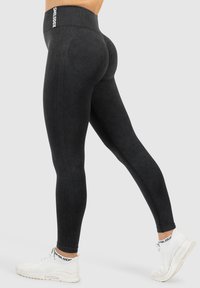 Czarne legginsy z wysokim stanem, z prążkowaną teksturą i wykończeniem przy szwie w kształcie łuku. W połączeniu z białymi butami sportowymi z logo na skarpetce.