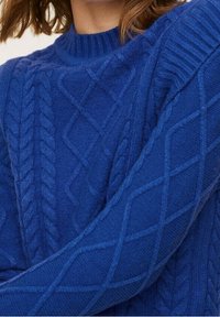 Pull bleu en maille torsadée avec un design épais et un col côtelé, présentant des motifs texturés et une apparence douce et confortable.