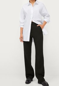 White button-up shirt, long-sleeved, untucked, paired with black wide-leg trousers. Shoes are black loafers. Smooth textures, basic patterns.