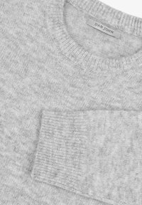 Suéter gris hecho de un material de punto suave, con un cuello redondo, puños acanalados y un pequeño bolsillo en el pecho. Textura sutil en todo su diseño.