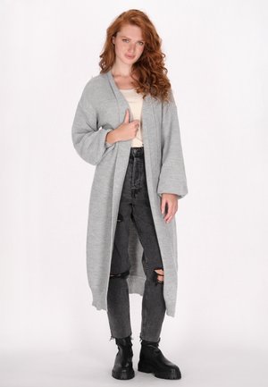 Cardigan lung gri tricotat, cu un model texturat, cu deschidere frontală și mâneci largi, asortat cu blugi negri ruptți și botoși negri până la gleznă.