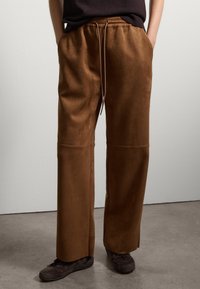 Pantalons en daim brun avec une coupe ample, une taille élastique et des poches avant, dotés d'une texture lisse et d'un design à jambes droites.
