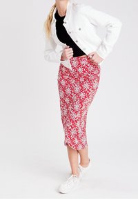 Jupe midi rouge à fleurs blanches, associée à un haut noir côtelé et une veste en denim blanche. Complétée par des baskets blanches.