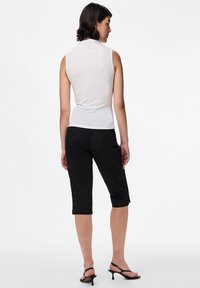 Biała, bezrękawnikowa bluzka w połączeniu z czarnymi, przyciętymi spodniami. Bluzka jest gładka i dopasowana, natomiast spodnie mają luźniejszy krój z kieszeniami.